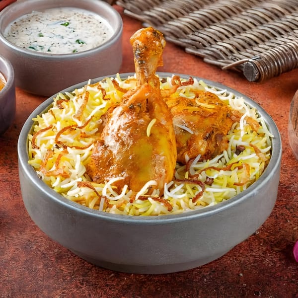 Chicken biryani with two chicken pieces, rice, fried onions, and a side of raita.