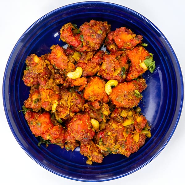 Spicy Indian chicken dish with cashews and herbs, served in a deep blue bowl.