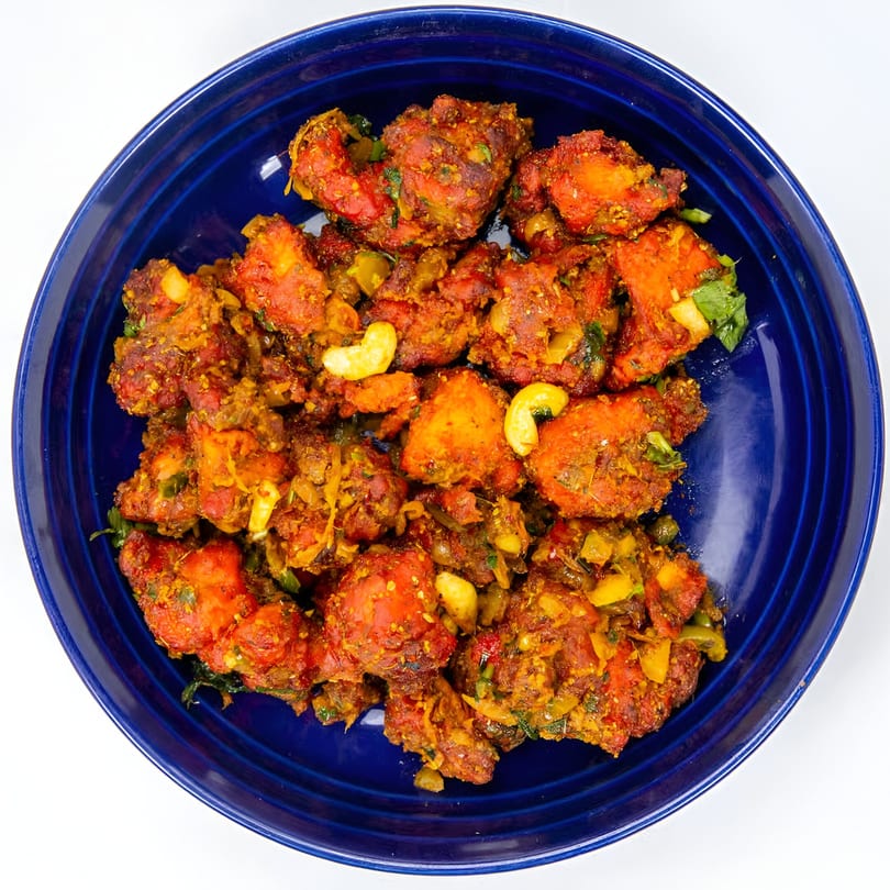 Spicy Indian chicken dish with cashews and herbs, served in a deep blue bowl.