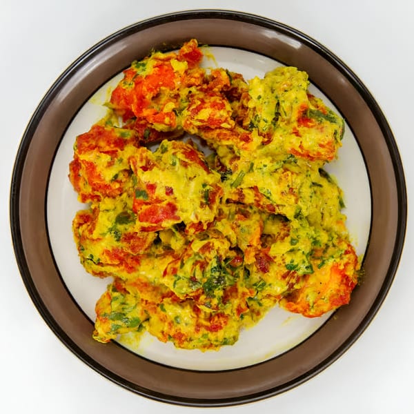 Overhead view of Indian chicken pakora, coated in a vibrant yellow and orange batter with green herbs.