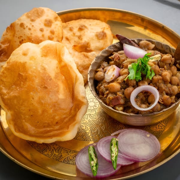 Golden puri bread and chana masala with red onion and green chili on a brass plate.