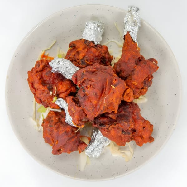 A plate of Indian chicken lollipops, deep-fried with a red spice coating and foil-wrapped bones.