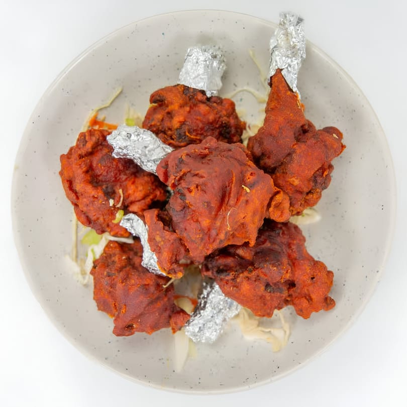 A plate of Indian chicken lollipops, deep-fried with a red spice coating and foil-wrapped bones.